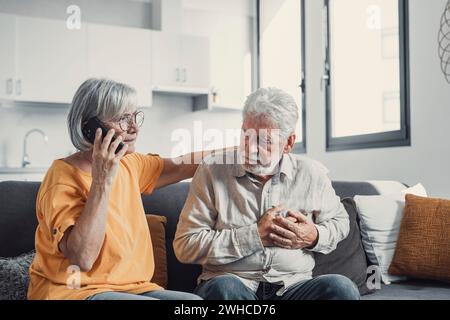 Femme mature, épouse appelant l'urgence, parlant au téléphone, tenant la main du vieux mari, homme aux cheveux gris ayant une crise cardiaque, touchant la poitrine, souffrant de Banque D'Images