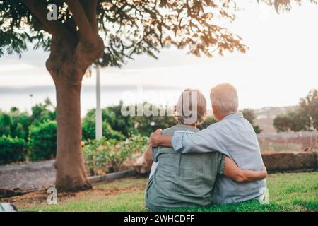 Portrait gros plan portrait heureux aux cheveux gris femme d'âge moyen blottie à son mari plus âgé souriant, profitant d'un moment tendre au parc. Lier aimant vieux couple de famille embrassant, regardant le coucher du soleil. Banque D'Images