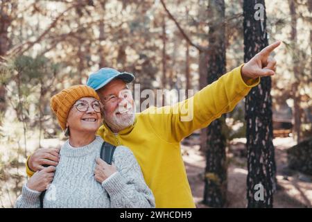 Portrait, gros plan de gens joyeux d'âge moyen souriant et regardant les arbres de la forêt autour d'eux. Couple actif de vieilles personnes âgées randonnant et marchant ensemble dans la montagne en s'amusant. Banque D'Images