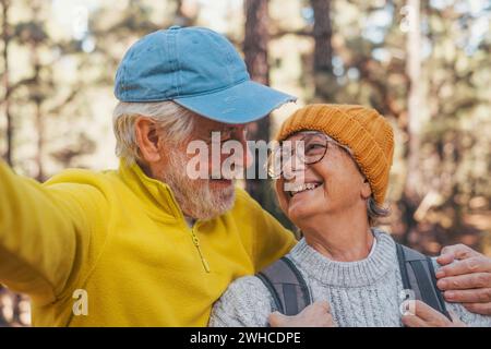 Portrait, gros plan d'un couple mignon de vieilles personnes âgées prenant un selfie ensemble dans la forêt de montagne regardant la caméra souriant en s'amusant. Deux personnes matures randonnant. Banque D'Images