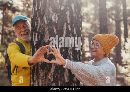 Portrait, gros plan de couple mignon de vieilles personnes âgées d'âge moyen faisant la forme de coeur autour de grand arbre aimant et prenant soin de la nature concept de style de vie. Deux personnes retraitées jouissant de plein air. Banque D'Images