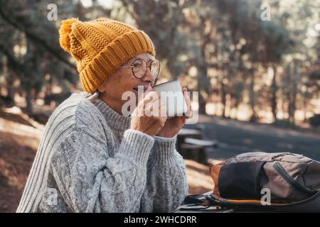 Portrait, gros plan de la femme d'âge moyen se relaxant boire du café ou du thé assis à table dans la forêt de montagne au milieu de la nature. Saison d'automne appréciant le style de vie conceptuel. Banque D'Images