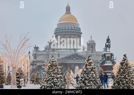 Russie, Saint-Pétersbourg, 30 décembre 2023 : les gens marchent parmi les arbres de Noël dans de fortes chutes de neige, un parc organisé en vacances près de se réunir La cathédrale d'Isaac Banque D'Images