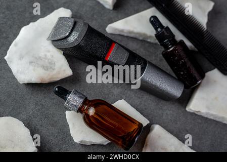 Articles de toilettage de barbe homme sur une surface de table en pierre, peigne, huile et tondeuse électrique Banque D'Images