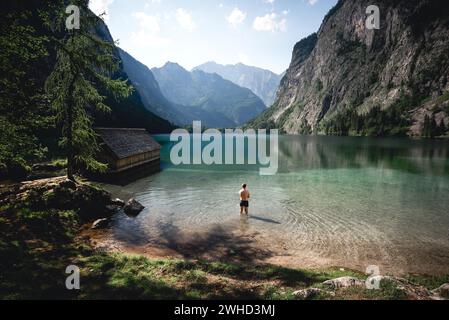 Homme debout au genou dans l'eau sur la rive de l'Obersee avec vue sur le massif Watzmann, Berchtesgaden Banque D'Images