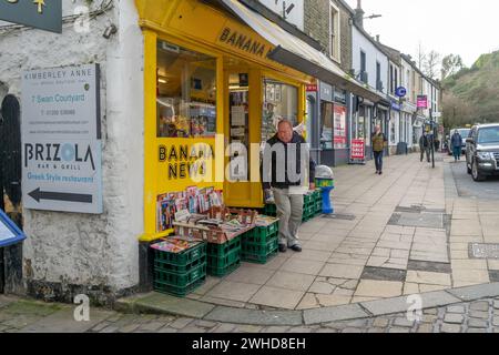 Un homme devant la façade peinte en jaune d'un marchand de journaux britannique traditionnel dans une petite ville de marché affichant des magazines et des journaux en vente Banque D'Images
