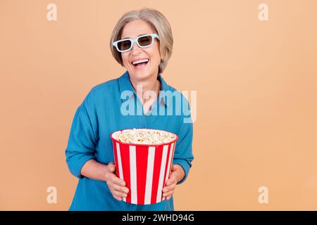 Portrait de la personne drôle avec les cheveux gris porter chemise élégante dans les lunettes 3d tenir la comédie de montre popcorn isolé sur fond de couleur beige Banque D'Images