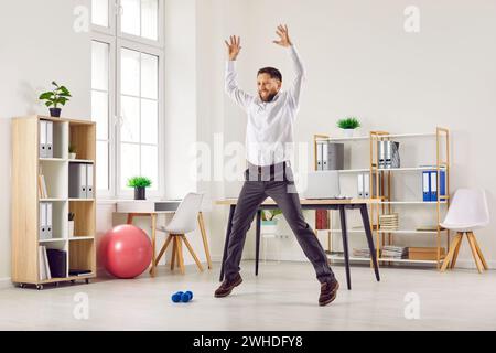 Heureux jeune employé faisant un exercice de saut pendant une séance d'entraînement de fitness dans le bureau Banque D'Images