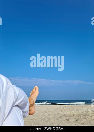 Pantalon en lin blanc avec pied de femme au premier plan, vue sur la mer et le ciel bleu, Markgrafenheide, mer Baltique, Allemagne Banque D'Images