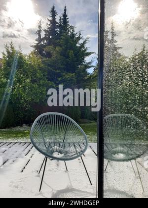 Vue à travers la fenêtre ouverte sur la terrasse dans la lumière du soleil couverte de neige aux arbres verts en arrière-plan dans le mois de mai sur le sujet du changement climatique Banque D'Images