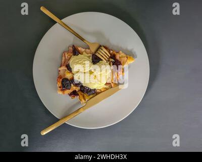 Une tranche de gâteau aux prunes avec de la glace à la vanille servie sur une assiette avec une fourchette et un couteau Banque D'Images