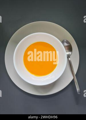 Soupe de citrouille fraîche maison servie pure dans un bol blanc sur une assiette grise avec une cuillère en argent Banque D'Images