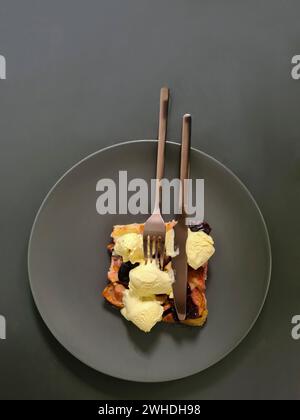 Une tranche de gâteau aux prunes avec de la glace à la vanille servie sur une assiette avec une fourchette et un couteau Banque D'Images