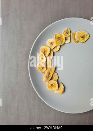 Chips de banane sur une assiette gris clair comme dessert et collation entre les repas Banque D'Images