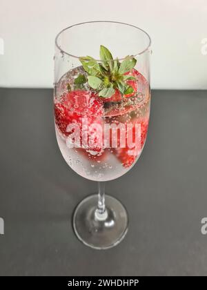 Fraises fraîches rouges entières mûres avec de l'eau minérale dans un verre de champagne comme boisson rafraîchissante sans alcool en été Banque D'Images