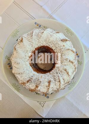 Gâteau rond de marbre avec du sucre blanc en poudre se tient sur une assiette avec une nappe blanche Banque D'Images