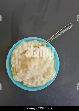 Pudding de riz avec cuillère dans un bol en verre sur un fond gris à la lumière du jour Banque D'Images