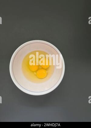 Trois œufs crus battus, blancs et jaunes d'œufs dans un bol blanc Banque D'Images