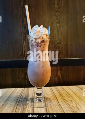 Chocolat glacé à la crème dans un grand verre avec une paille et une cuillère est élégamment disposé sur une table dans le restaurant Banque D'Images