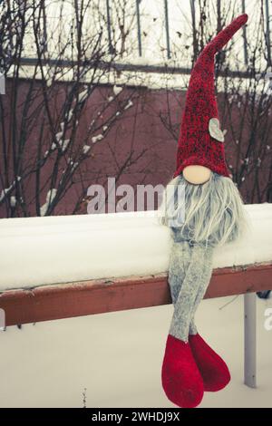 Nain avec symbole de coeur sur le banc dans la neige. Cadeau romantique. Concept de la Saint-Valentin. GNOME avec coeur et chapeau rouge dans la neige. Fond d'amour. Banque D'Images