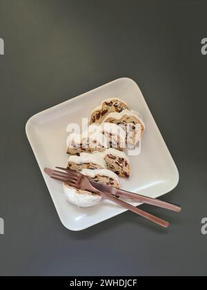 Plusieurs morceaux de gâteau de Noël reposent sur une assiette carrée en porcelaine blanche avec des couverts Banque D'Images