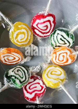 Huit sucettes colorées sont encore enveloppées dans une feuille de plastique en cercle dans un bol gris Banque D'Images