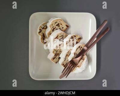 Plusieurs morceaux de gâteau de Noël reposent sur une assiette carrée en porcelaine blanche avec des couverts Banque D'Images