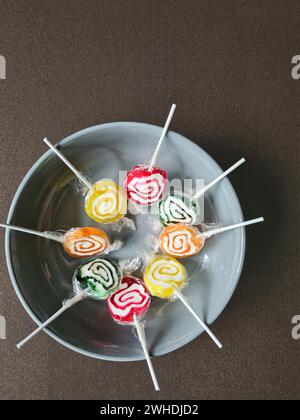 Huit sucettes sont encore enveloppées dans une feuille de plastique dans un cercle sur un bol blanc Banque D'Images