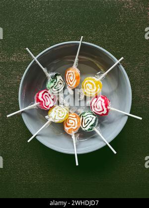 Huit sucettes colorées sont encore enveloppées dans une feuille de plastique en cercle dans un bol gris Banque D'Images
