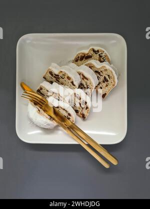 Plusieurs morceaux de gâteau de Noël reposent sur une assiette carrée en porcelaine blanche avec des couverts dorés dans la saison de l'Avent avant Noël Banque D'Images