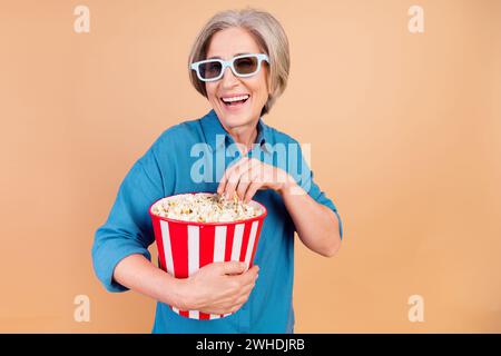 Portrait de la personne de bonne humeur avec les cheveux gris blancs porter chemise élégante manger popcorn montre film de comédie isolé sur fond de couleur beige Banque D'Images