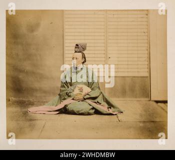 Un homme, peut-être un fonctionnaire du gouvernement, tenant un éventail, assis, face à gauche, portant un chapeau en forme de couronne....Japon coloré à la main avec aquarelle Photographic Print vers les années 1870 Banque D'Images