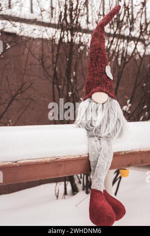 Nain avec symbole de coeur sur le banc dans la neige. Cadeau romantique. Concept de la Saint-Valentin. GNOME avec coeur et chapeau rouge dans la neige. Fond d'amour. Banque D'Images