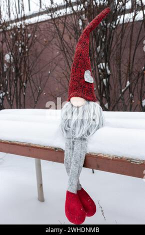 Nain avec symbole de coeur sur le banc dans la neige. Cadeau romantique. Concept de la Saint-Valentin. GNOME avec coeur et chapeau rouge dans la neige. Fond d'amour. Banque D'Images