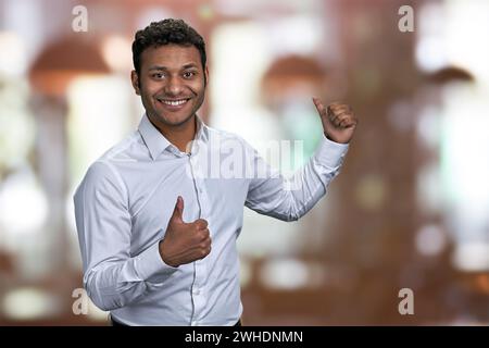 Gars joyeux pointant sur l'espace de copie derrière son dos. Homme indien pointant avec le pouce sur l'espace de copie. Place pour votre publicité. Banque D'Images