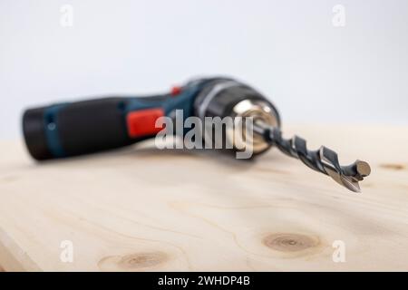 Travail du bois, perceuse sans fil avec foret métal à bois inséré 10 mm, point central, flou, repose sur le panneau de bois collé, Banque D'Images