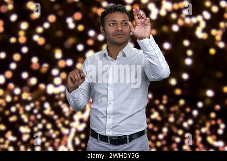 Jeune homme d'affaires indien attrayant travaillant sur l'interface invisible. Lumières bokeh festives en arrière-plan. Banque D'Images