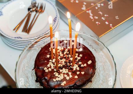 Gâteau au chocolat avec quatre bougies allumées sur une table blanche. Banque D'Images