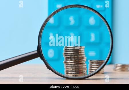 Une pile de pièces de monnaie en métal et une loupe en plastique sur fond bleu. Le concept de l'augmentation des impôts, des subventions Banque D'Images