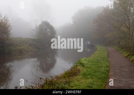 En regardant vers le bas du chemin de halage du canal Trent et Mersey, il y a un bateau étroit amarré au loin. Le temps est brumeux Banque D'Images