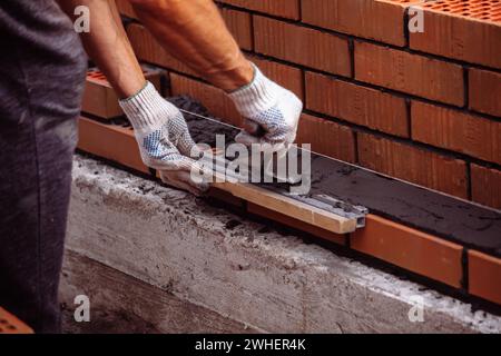 Truelles de constructeur frottent le mortier de ciment sur la brique pendant la brique. Banque D'Images