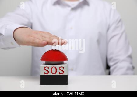 Homme appuyant sur le bouton rouge SOS à la table blanche, gros plan Banque D'Images