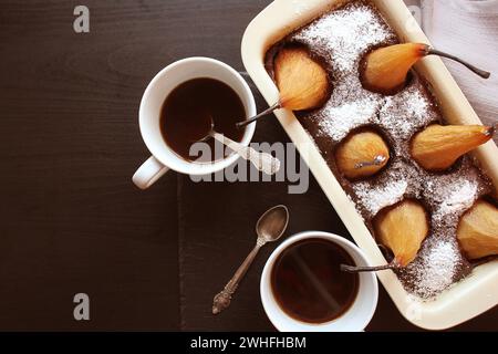 Gâteau de pain au chocolat avec des poires entières cuites à l'intérieur et deux tasses de café sur fond sombre. Vue d'en haut Banque D'Images