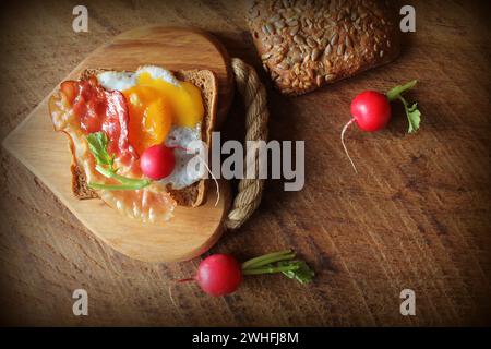 Petit-déjeuner , croustillant de bacon, d'œufs au plat et du pain. Sandwich sur une planche à découper. Table rustique . Vue d'en haut Banque D'Images