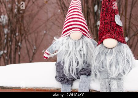 Couple de nains sur le banc dans la neige. Cadeau romantique. Concept d'amitié. Concept de la Saint-Valentin. Gnomes avec coeur et chapeau rouge dans la neige. Banque D'Images