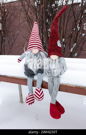 Couple de nains sur le banc dans la neige. Cadeau romantique. Concept d'amitié. Concept de la Saint-Valentin. Gnomes avec coeur et chapeau rouge dans la neige. Banque D'Images