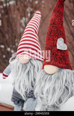 Couple de nains sur le banc dans la neige. Cadeau romantique. Concept d'amitié. Concept de la Saint-Valentin. Gnomes avec coeur et chapeau rouge dans la neige. Banque D'Images