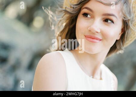 Femme souriante dans un chapeau de paille avec ses cheveux soufflant dans le vent. Portrait Banque D'Images