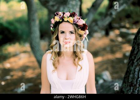 Mariée dans une couronne de fleurs multicolores sur sa tête se tient près d'un arbre Banque D'Images