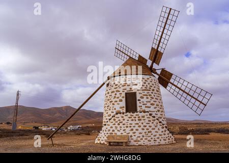 Un moulin à vent traditionnel se dresse contre un ciel nuageux dans le paysage rustique de Valles de Ortega, Fuerteventura. Banque D'Images